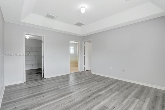 unfurnished bedroom featuring ensuite bathroom, light hardwood / wood-style flooring, a walk in closet, a tray ceiling, and a closet