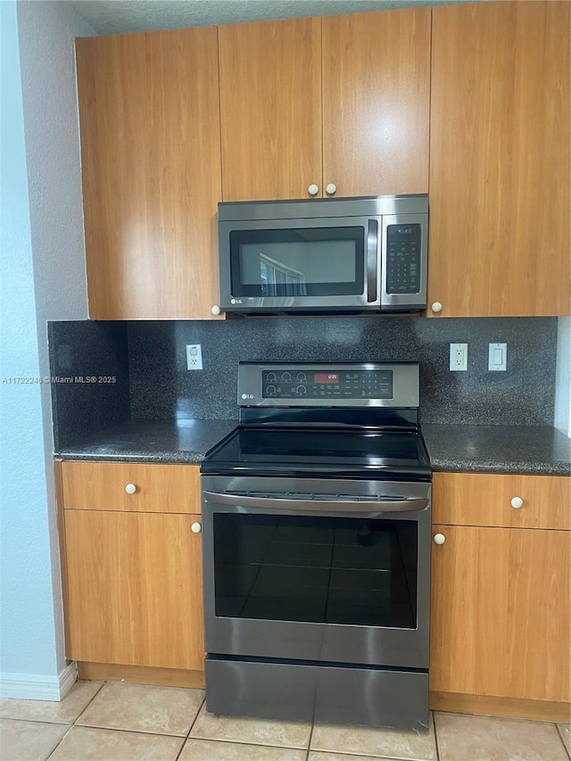 kitchen featuring light tile patterned floors, stainless steel appliances, tasteful backsplash, and dark stone countertops