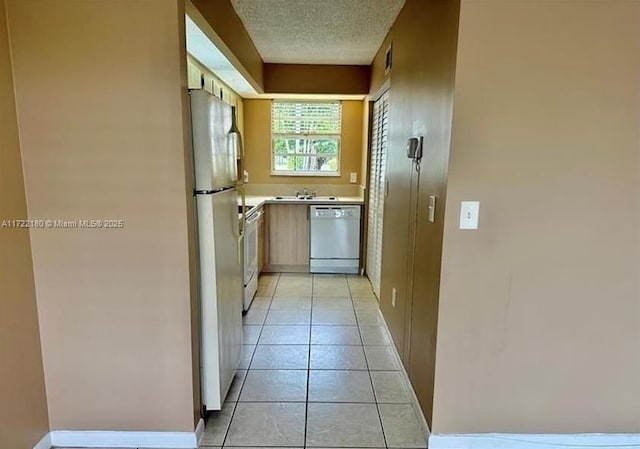 kitchen with a textured ceiling, sink, light tile patterned floors, and white appliances