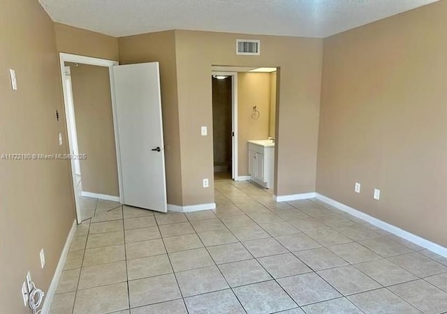 unfurnished bedroom featuring a textured ceiling, ensuite bathroom, and light tile patterned flooring