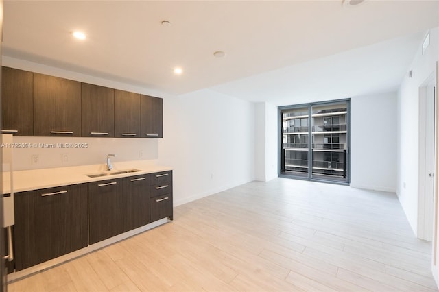 kitchen with dark brown cabinets, sink, and light hardwood / wood-style flooring