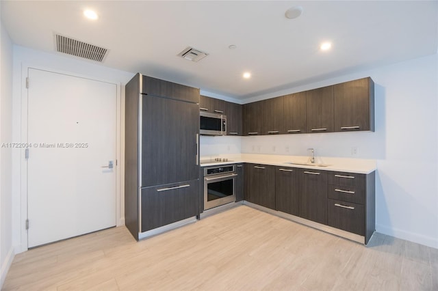 kitchen featuring sink, stainless steel appliances, dark brown cabinets, and light hardwood / wood-style floors