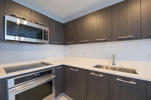 kitchen with appliances with stainless steel finishes, dark brown cabinets, and sink