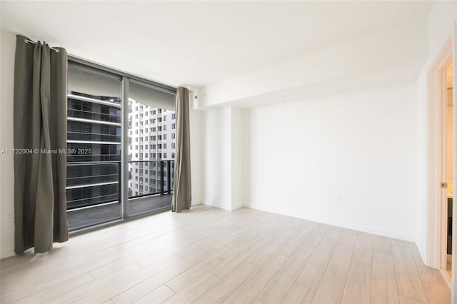 spare room with floor to ceiling windows and light hardwood / wood-style flooring