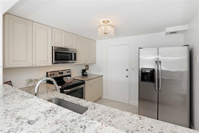 kitchen with light stone counters, stainless steel appliances, sink, an inviting chandelier, and light tile patterned flooring