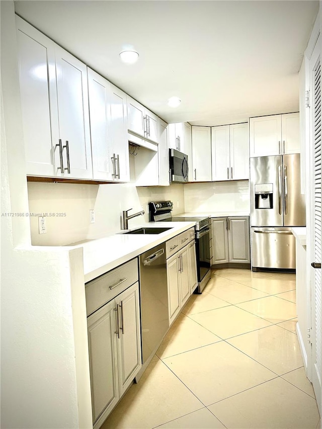 kitchen with appliances with stainless steel finishes, white cabinetry, light tile patterned floors, and sink