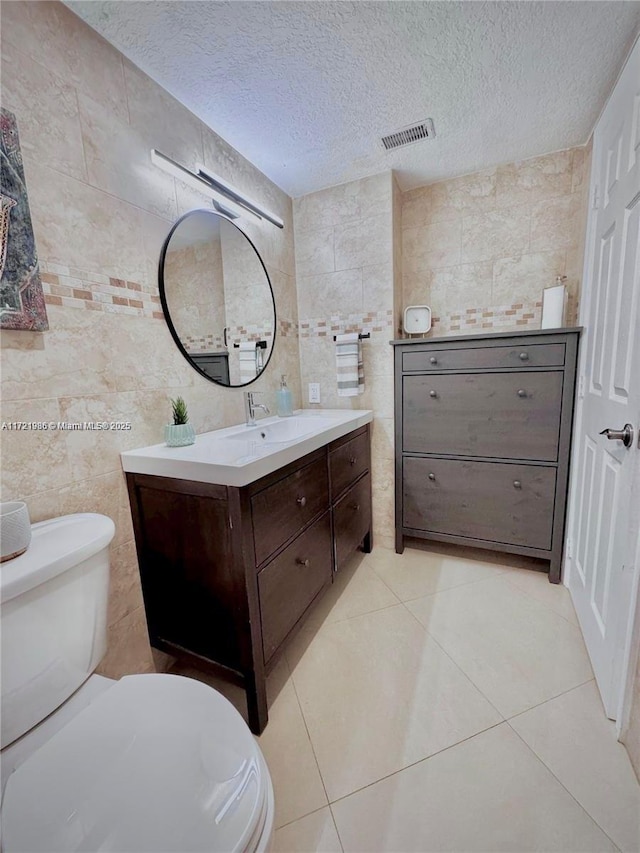 bathroom with tile patterned floors, a textured ceiling, vanity, tile walls, and toilet