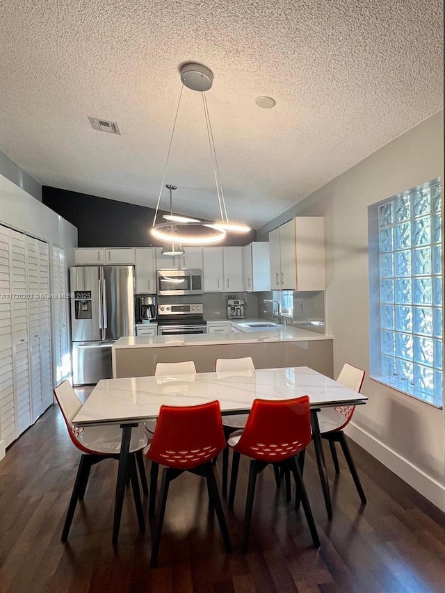 kitchen with appliances with stainless steel finishes, decorative light fixtures, dark hardwood / wood-style flooring, white cabinets, and sink