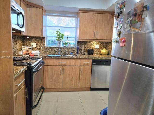 kitchen featuring light tile patterned floors, stone countertops, a sink, appliances with stainless steel finishes, and tasteful backsplash