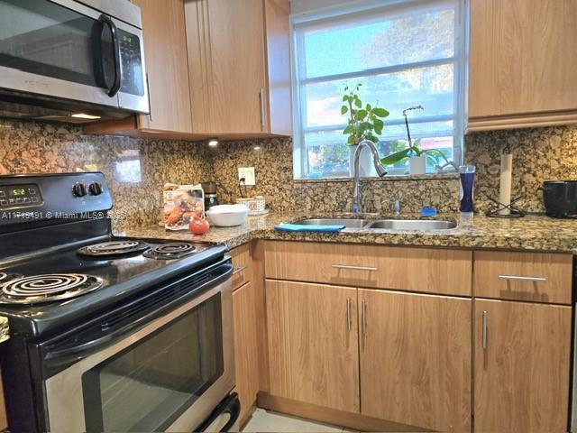 kitchen with appliances with stainless steel finishes, a sink, light stone counters, and tasteful backsplash