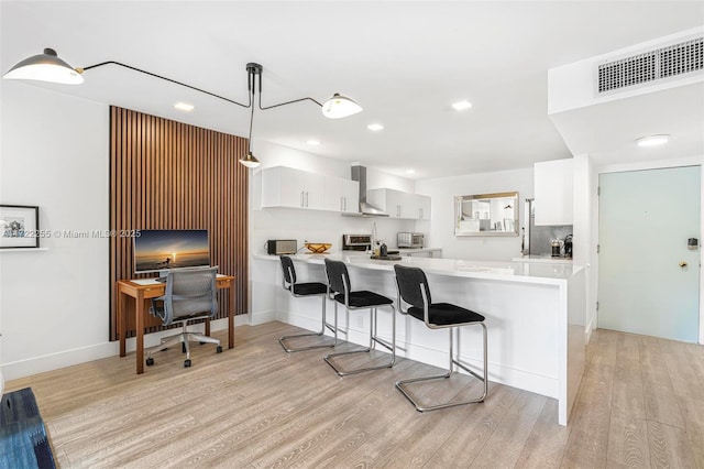 kitchen featuring wall chimney exhaust hood, white cabinetry, kitchen peninsula, and hanging light fixtures