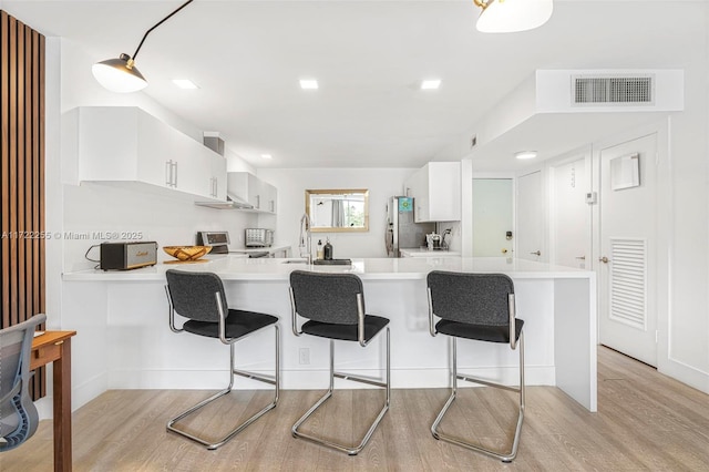 kitchen featuring stainless steel fridge, white cabinetry, light wood-type flooring, and kitchen peninsula