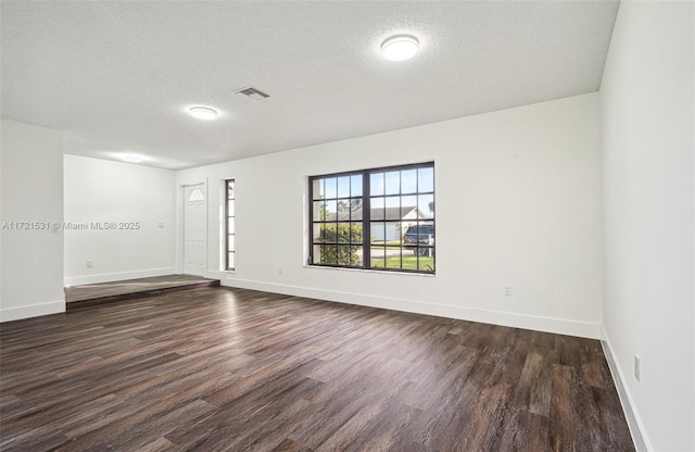 empty room with dark hardwood / wood-style flooring and a textured ceiling