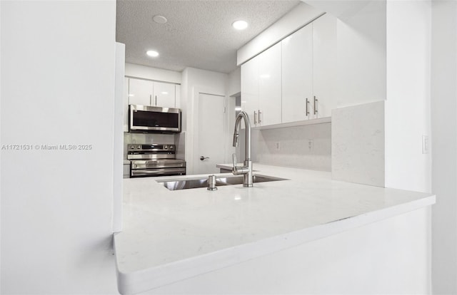 kitchen featuring sink, kitchen peninsula, a textured ceiling, white cabinets, and appliances with stainless steel finishes