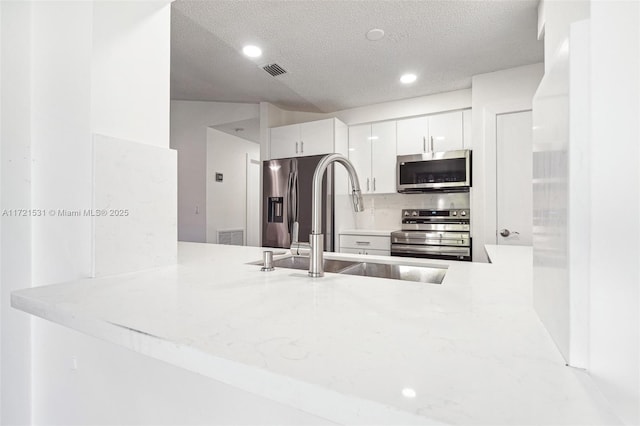 kitchen featuring kitchen peninsula, a textured ceiling, stainless steel appliances, sink, and white cabinets