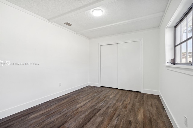 unfurnished bedroom featuring beam ceiling, dark wood-type flooring, a textured ceiling, and a closet