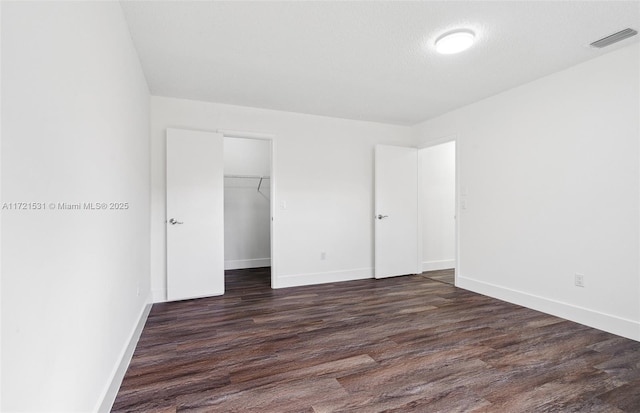 unfurnished bedroom with a textured ceiling, a walk in closet, a closet, and dark wood-type flooring