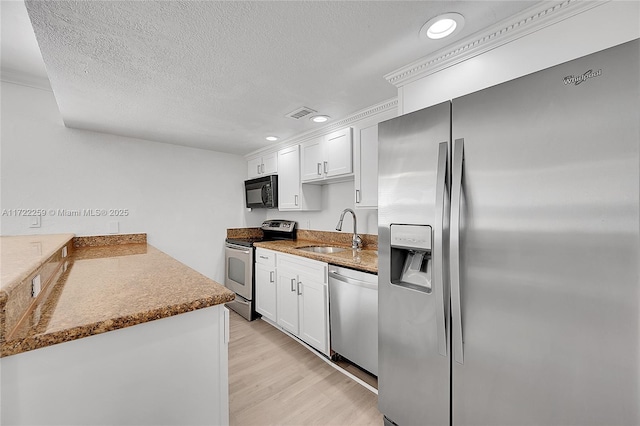 kitchen featuring sink, appliances with stainless steel finishes, white cabinetry, light hardwood / wood-style floors, and a textured ceiling