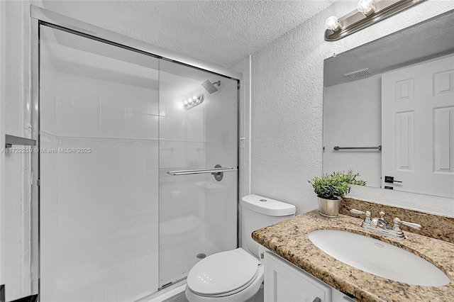 bathroom with a shower with door, vanity, a textured ceiling, and toilet