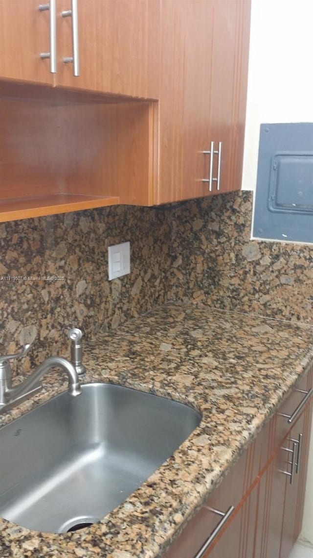 details with backsplash, electric panel, dark stone countertops, and sink