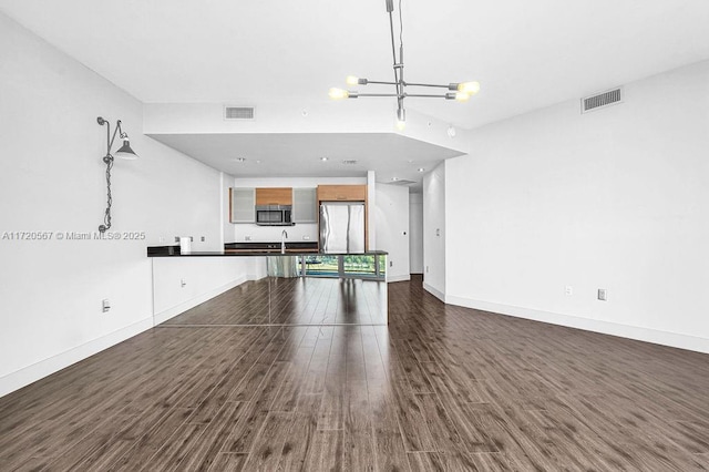 unfurnished living room with sink, dark hardwood / wood-style floors, and a notable chandelier