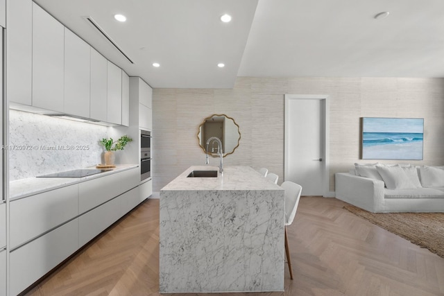 kitchen with a kitchen island with sink, sink, light parquet floors, and white cabinets