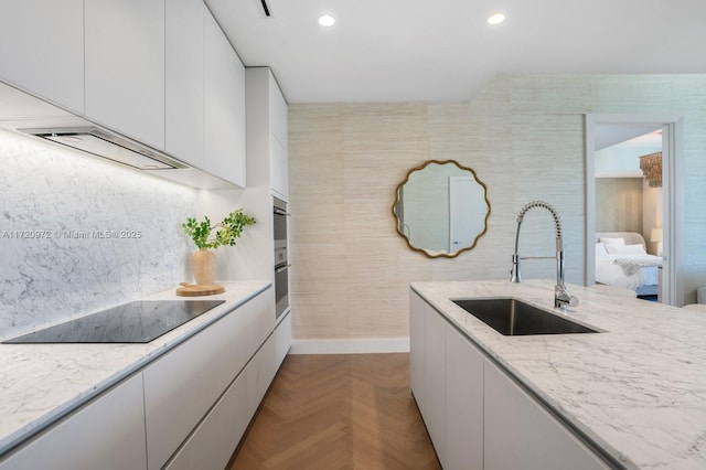 kitchen featuring sink, black electric cooktop, light parquet flooring, light stone countertops, and white cabinets