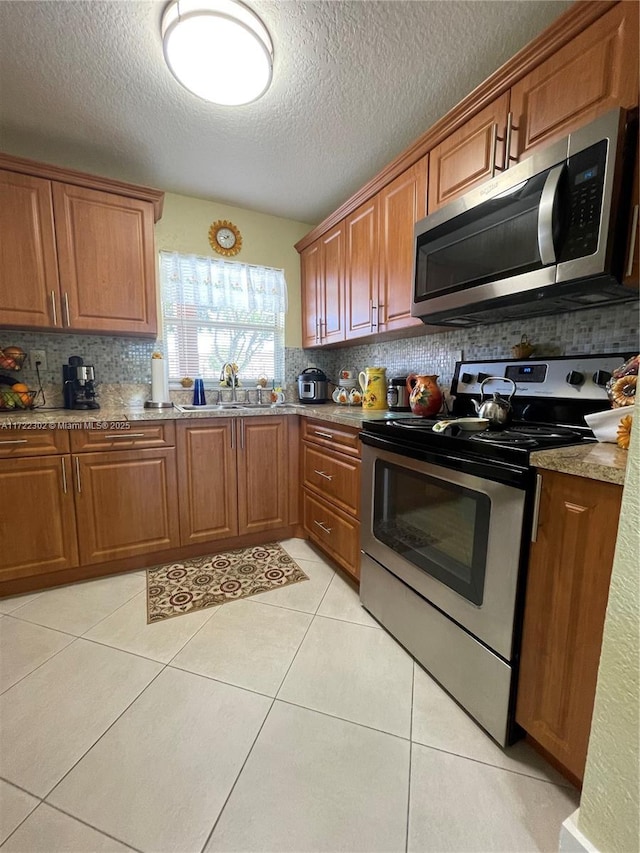 kitchen featuring sink, a textured ceiling, tasteful backsplash, light tile patterned flooring, and stainless steel appliances