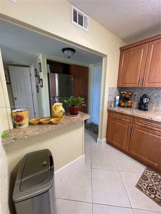 kitchen featuring stainless steel refrigerator, light stone countertops, a textured ceiling, decorative backsplash, and light tile patterned flooring