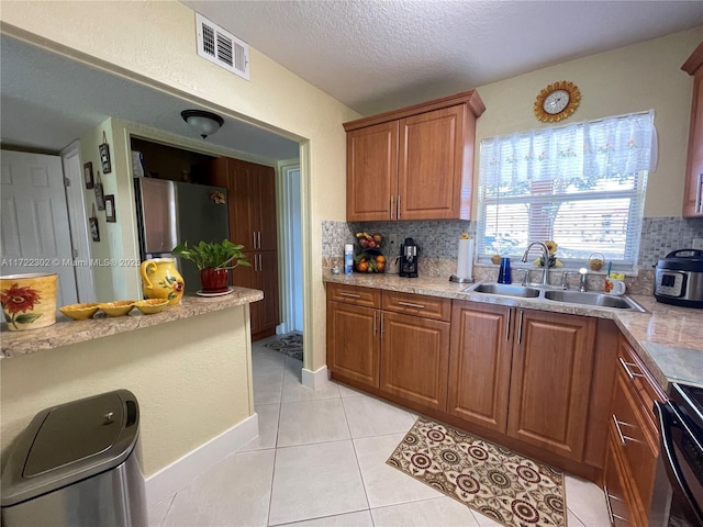 kitchen with decorative backsplash, a textured ceiling, sink, light tile patterned floors, and range