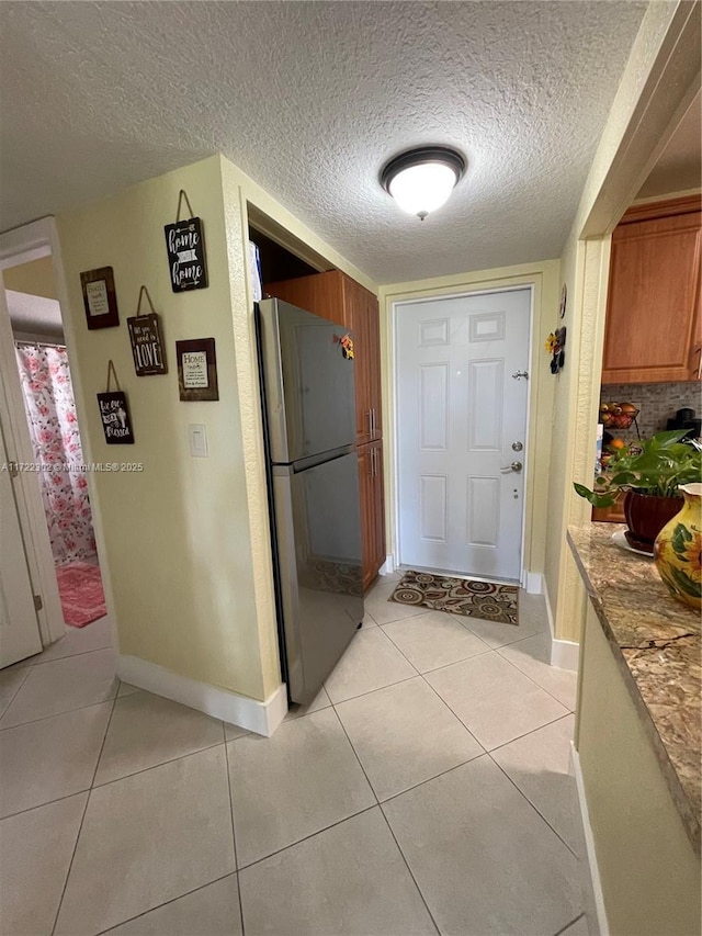 kitchen featuring stainless steel refrigerator, light tile patterned floors, and a textured ceiling