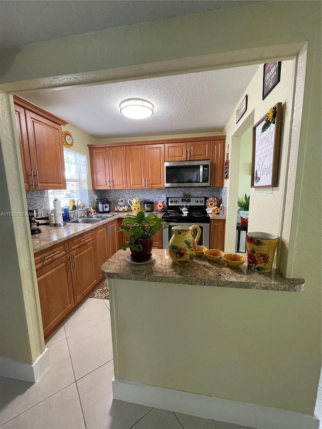 kitchen with sink, backsplash, a textured ceiling, light tile patterned flooring, and appliances with stainless steel finishes