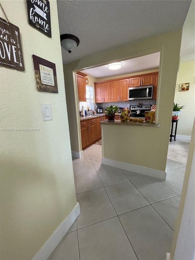 kitchen featuring tasteful backsplash, kitchen peninsula, a textured ceiling, light tile patterned floors, and appliances with stainless steel finishes