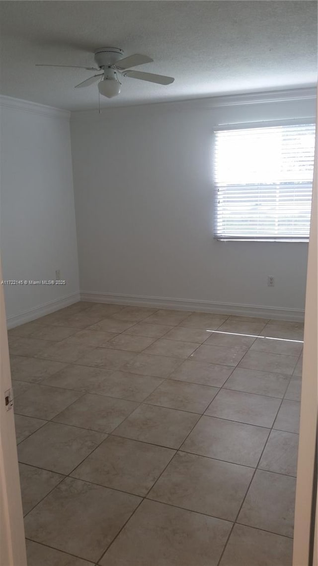 tiled empty room featuring ceiling fan and ornamental molding