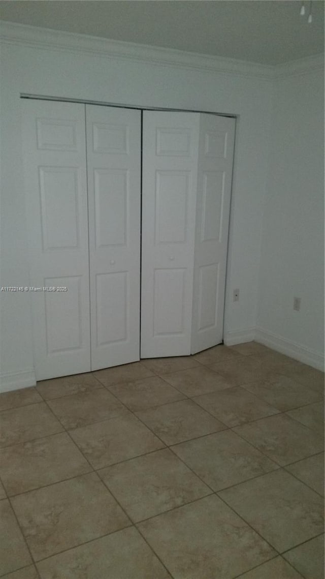 unfurnished bedroom with a closet, light tile patterned flooring, and ornamental molding