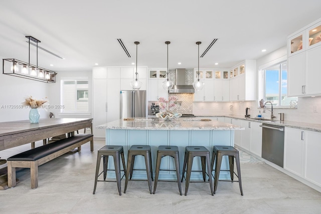 kitchen with light stone countertops, appliances with stainless steel finishes, a center island, and wall chimney range hood