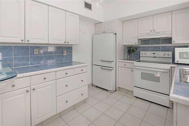 kitchen featuring white appliances, white cabinets, decorative backsplash, light tile patterned floors, and tile counters