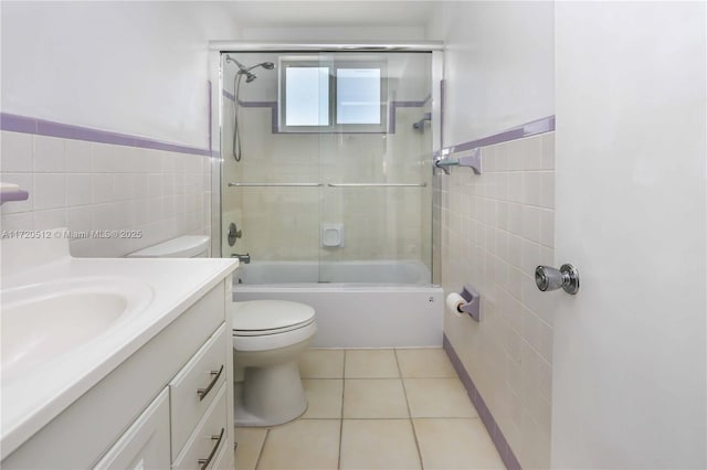 full bathroom featuring combined bath / shower with glass door, tile patterned floors, toilet, vanity, and tile walls