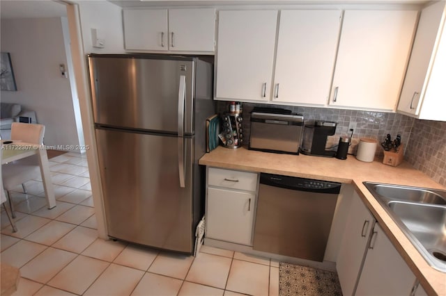 kitchen with appliances with stainless steel finishes, light tile patterned floors, decorative backsplash, white cabinets, and sink