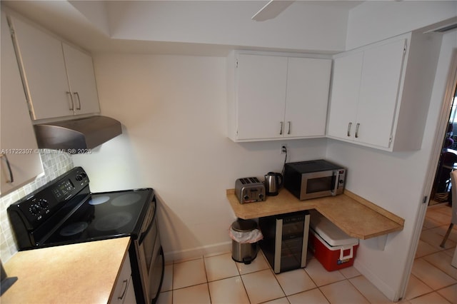 kitchen featuring ventilation hood, light tile patterned floors, black electric range, and white cabinetry