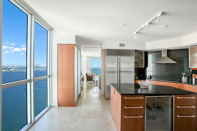 kitchen featuring a water view, wall chimney range hood, wine cooler, built in refrigerator, and a wall of windows