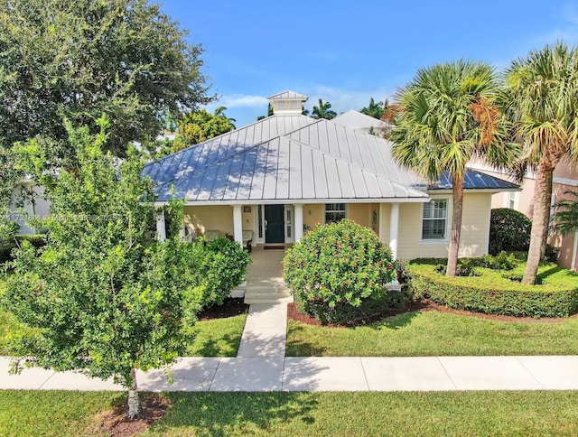 view of front facade with metal roof, a standing seam roof, a front yard, and stucco siding