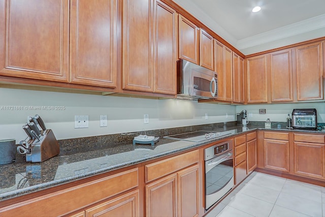 kitchen featuring appliances with stainless steel finishes, brown cabinetry, dark stone countertops, and ornamental molding