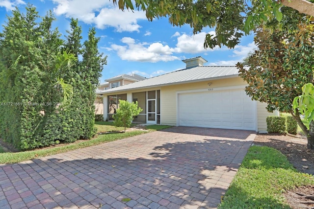 view of front of property featuring a garage, a sunroom, metal roof, and decorative driveway