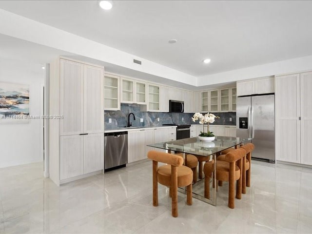 kitchen featuring stainless steel appliances, a sink, a kitchen island, decorative backsplash, and glass insert cabinets