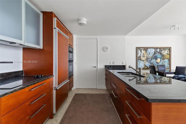 kitchen featuring cooktop, double oven, dark stone counters, and sink