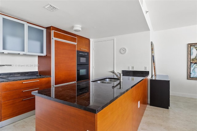 kitchen with dark stone counters, paneled fridge, black double oven, sink, and light tile patterned floors