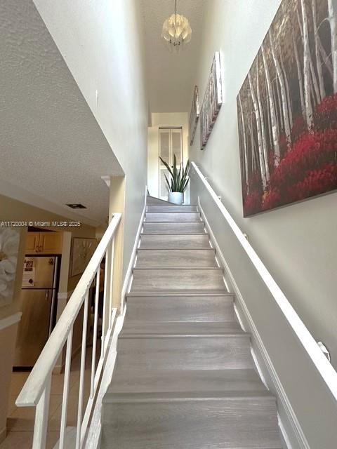 stairway with a textured ceiling and a notable chandelier