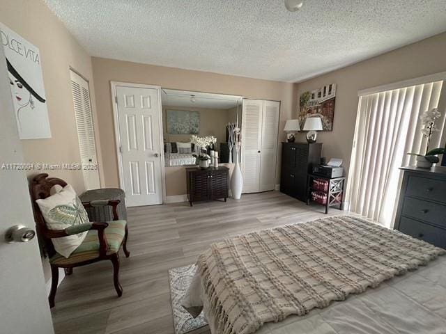 bedroom with a textured ceiling, light hardwood / wood-style floors, and multiple closets