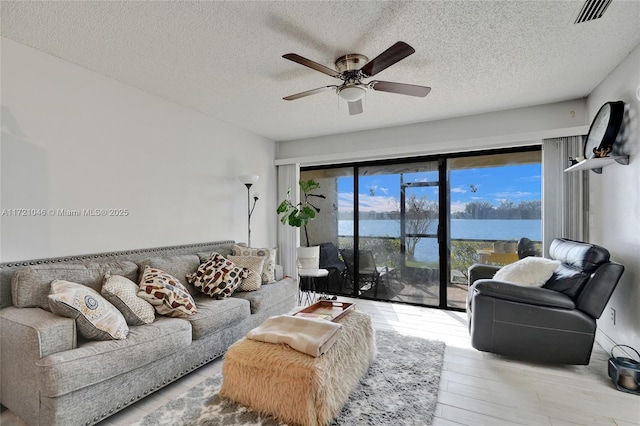 living room featuring ceiling fan, a water view, a textured ceiling, and light hardwood / wood-style flooring